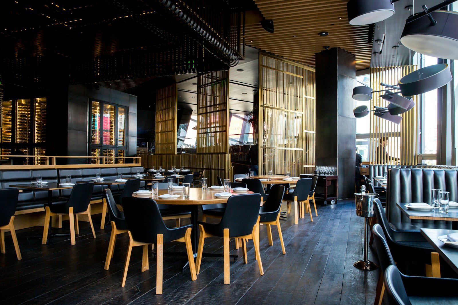 Warmly lit restaurant bar with rows of bottles on backlit shelves and a polished wood counter in the foreground